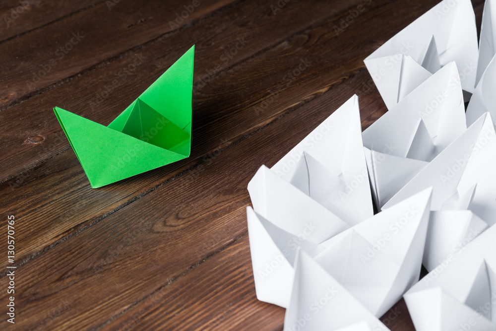 Business leadership concept with white and color paper boats on wooden table