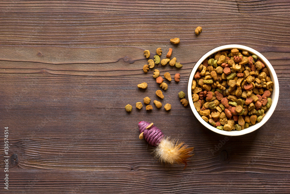 dry cat food in bowl on wooden background top view