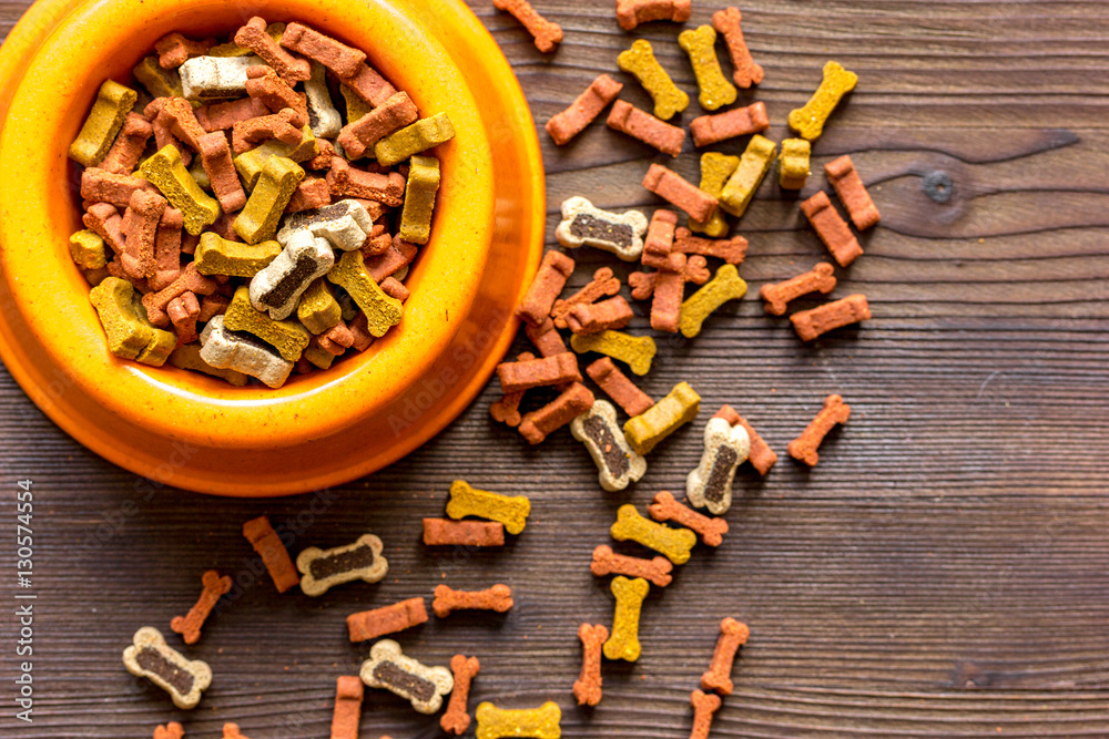 dry dog food in bowl on wooden background top view