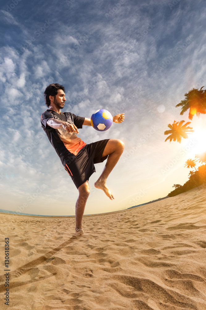 Beach soccer player in action. Sunny beach wide angle and sea