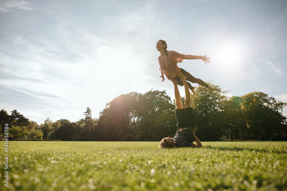 Healthy young couple doing acrobatic yoga at park