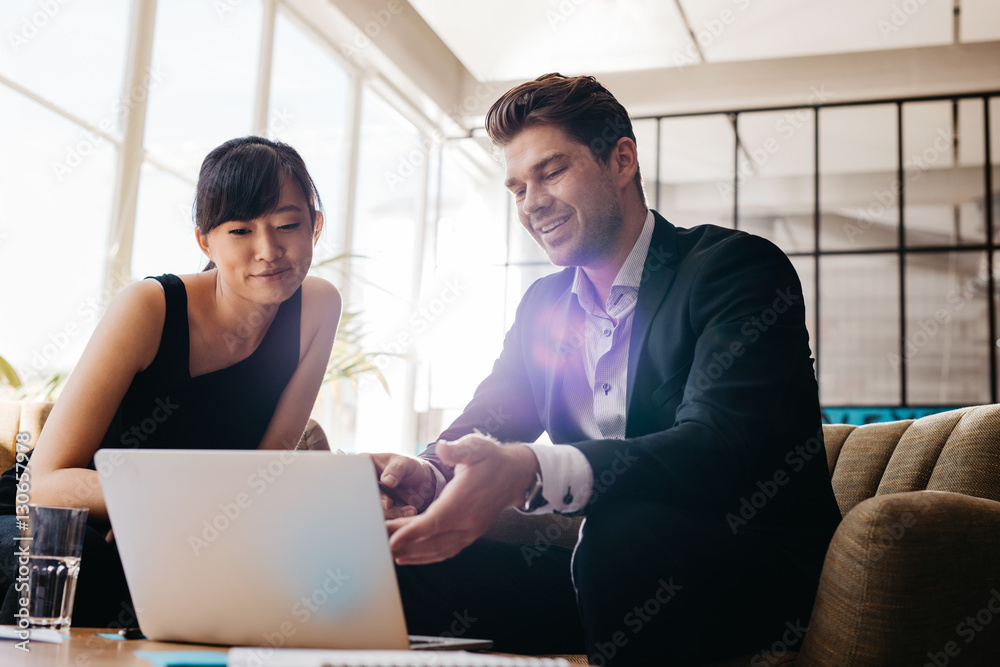 two businesspeople using laptop in lobby of modern office