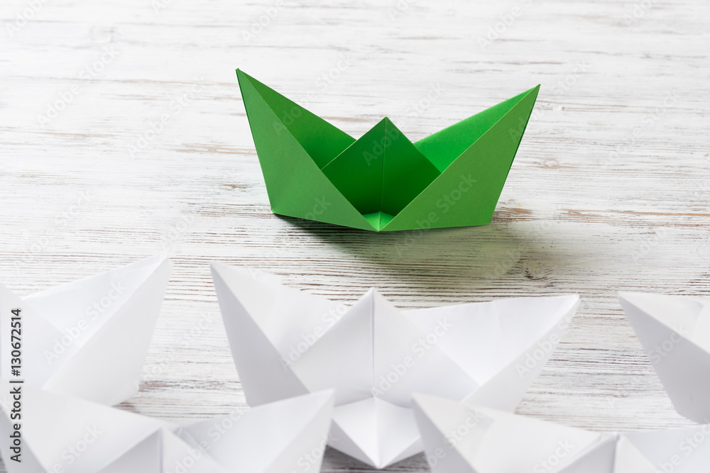 Business leadership concept with white and color paper boats on wooden table