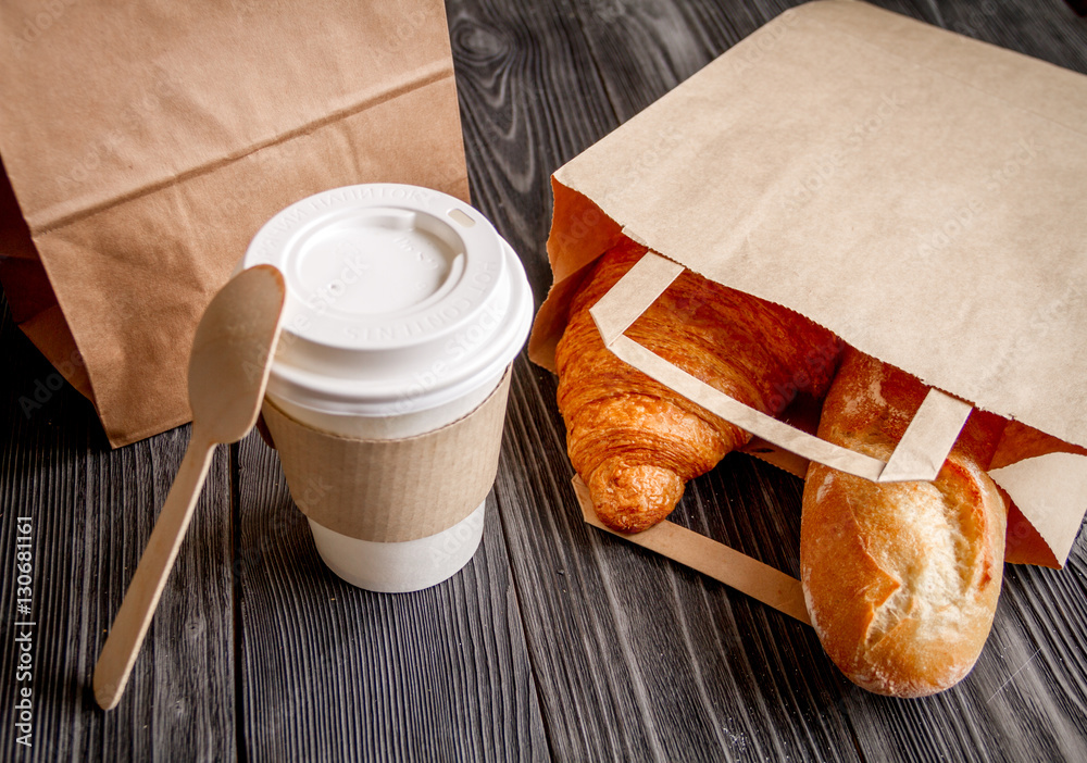 cup coffee and croissant in paper bag on wooden background