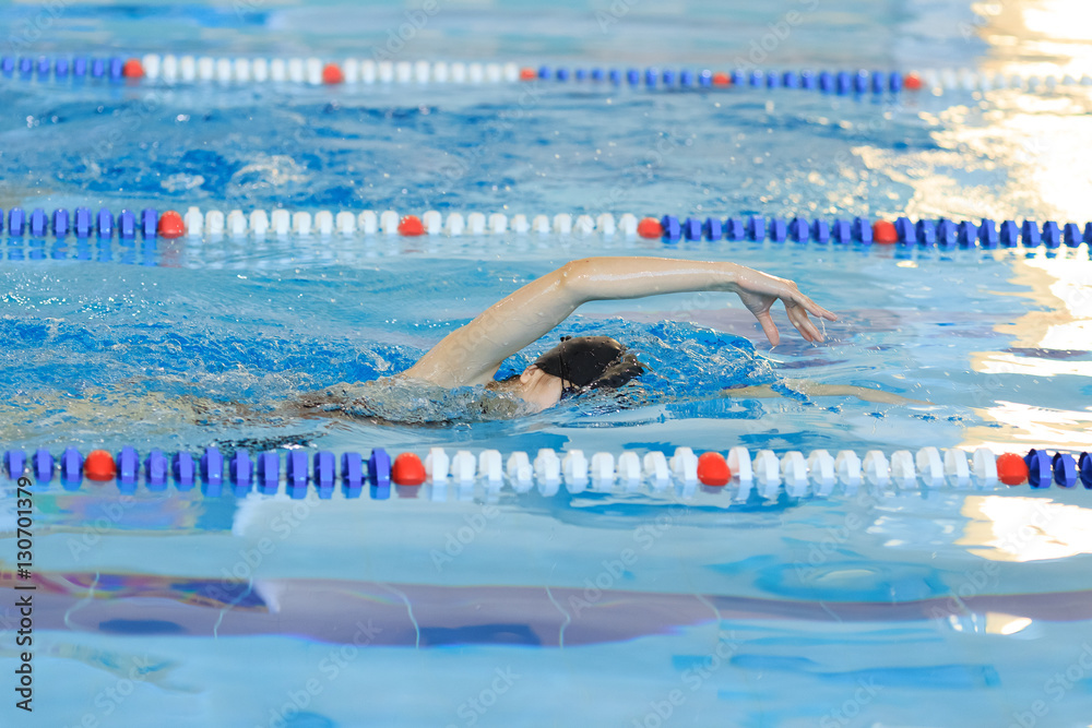 Young girl in goggles and cap swimming front crawl stroke style in the blue water pool.