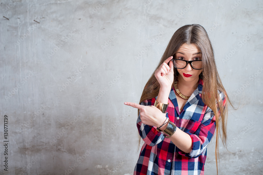 Portrait of watchful woman in the red checkered shirt with eyeglasses on the gray textured wall back