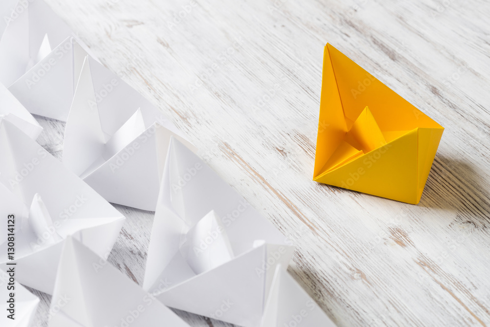 Business leadership concept with white and color paper boats on wooden table