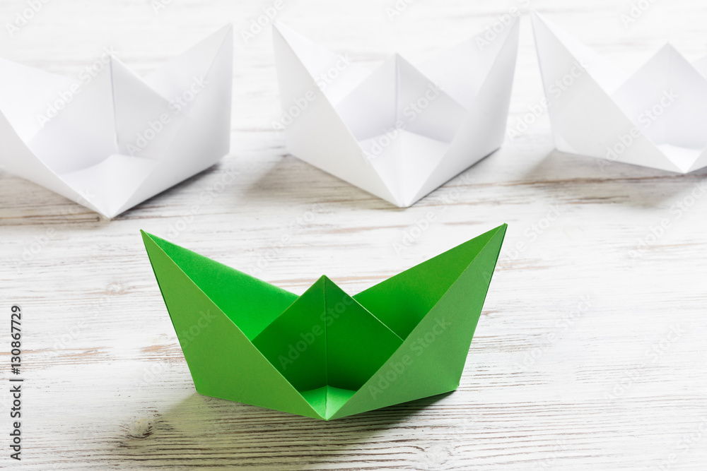 Business leadership concept with white and color paper boats on wooden table