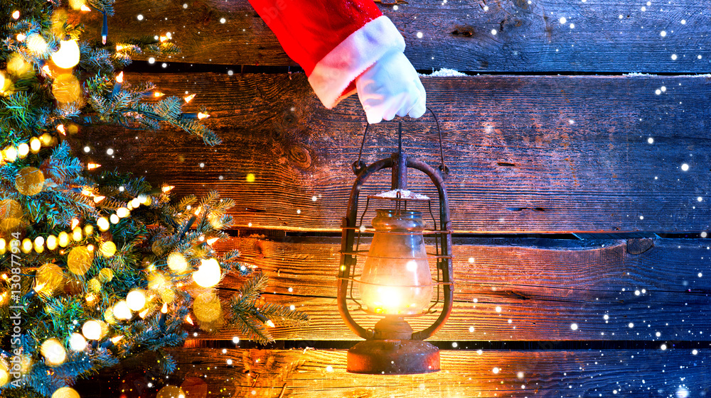 Christmas scene. Santas hand holding vintage oil lamp over wooden background