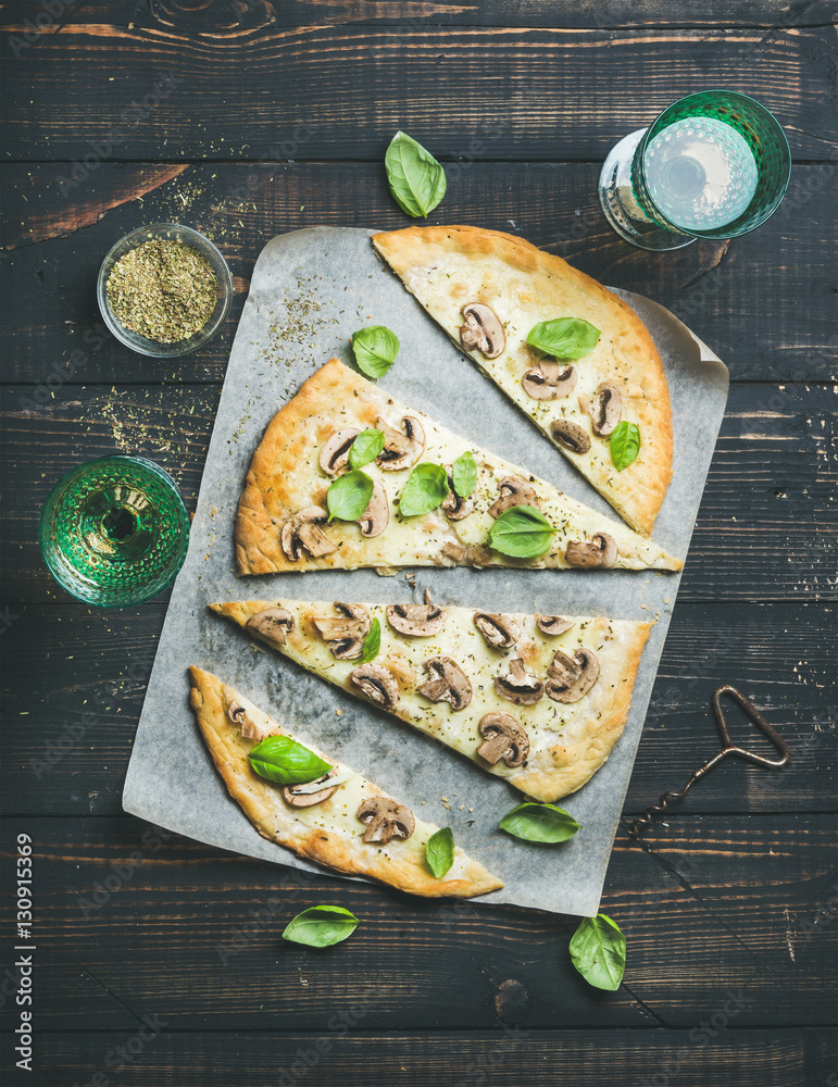 Homemade mushroom pizza with basil cut in slices, spices in glass and rose wine on dark scorched woo