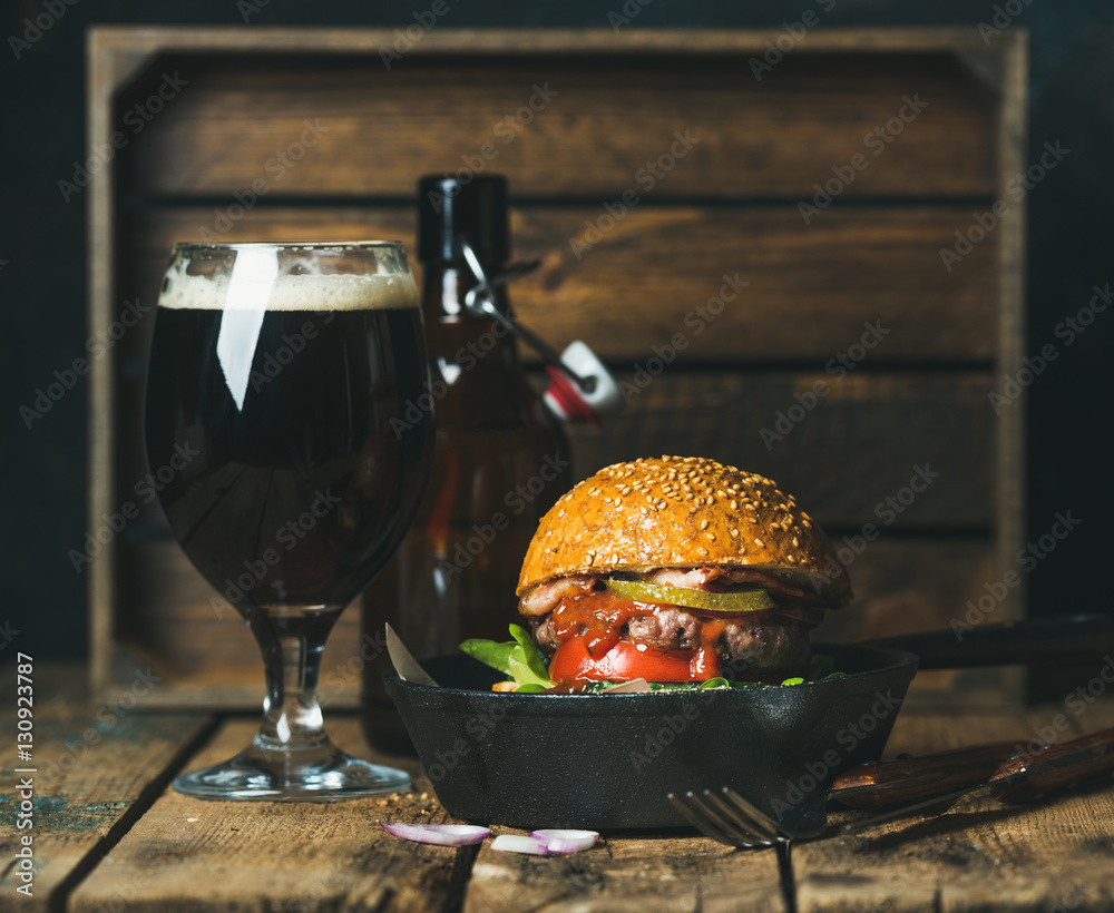 Homemade beef burger with crispy bacon, fresh vegetables and tomato sauce in black cast iron pan ser