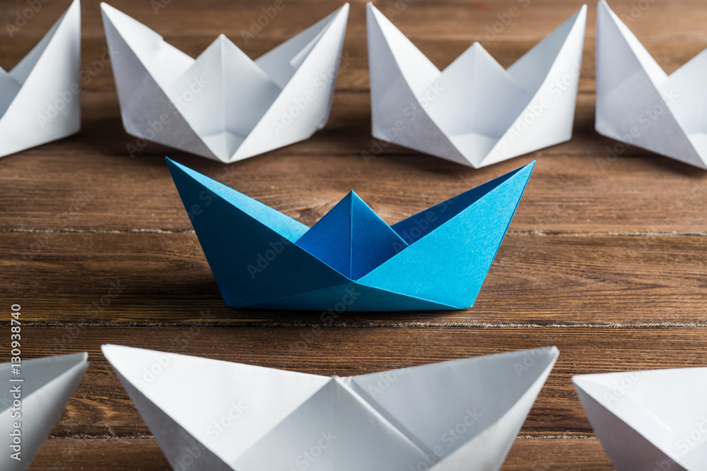 Business leadership concept with white and color paper boats on wooden table