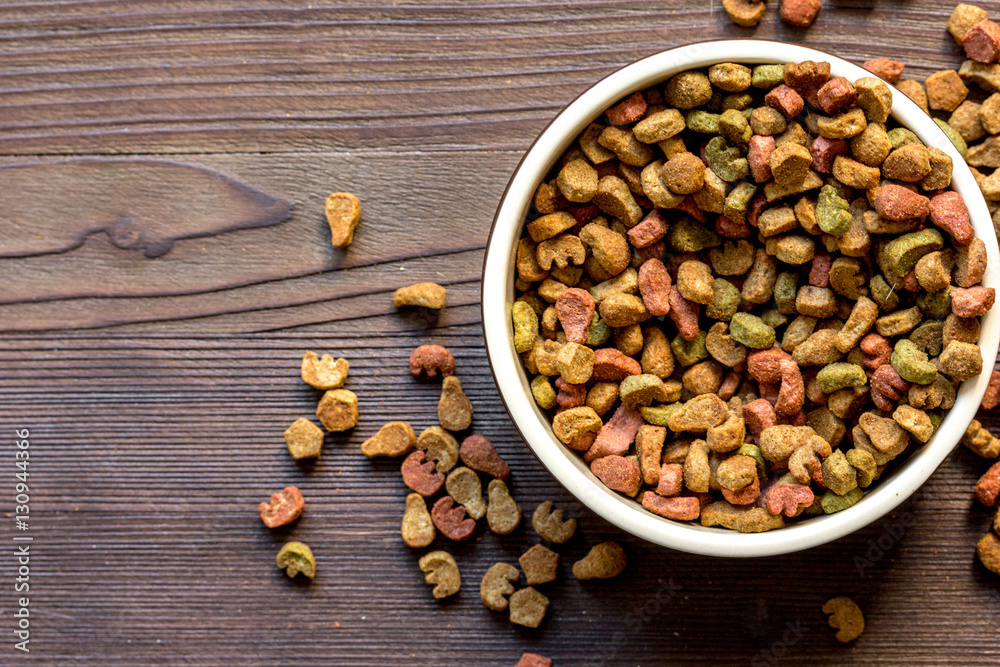 dry cat food in bowl on wooden background top view