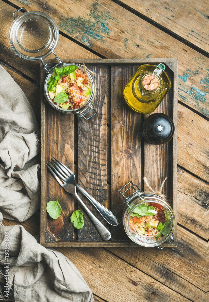 Healthy glass jar quinoa salad with cherry and sun-dried tomatoes, avocado, basil in wooden box over