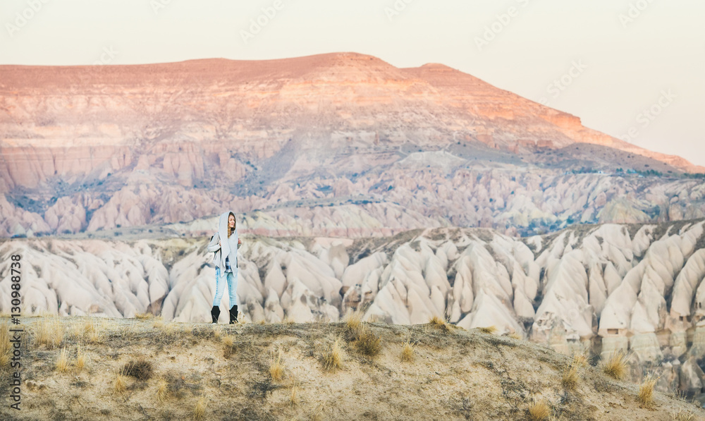 Young woman traveller in hood hiking in the mountains among natural rocks of Cappadocia, Central Tur