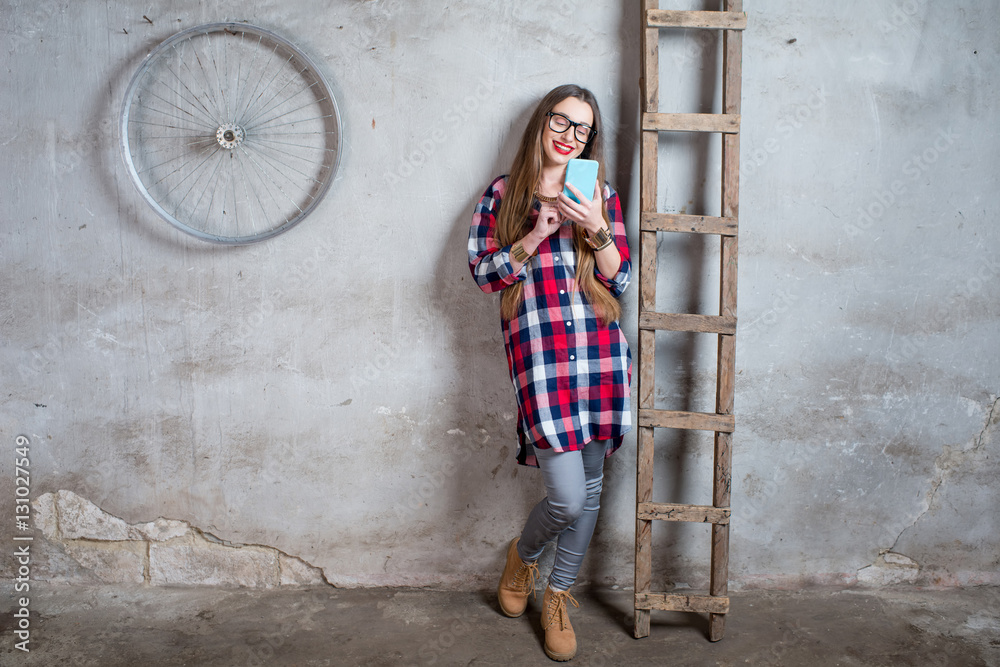 Young woman in checkered shirt standing in the old room with ladder on the gray textured wall backgr