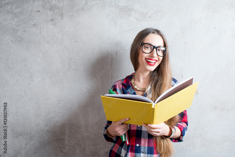 Portrait of a happy young student in checkered shirt with colorful books on the gray wall background