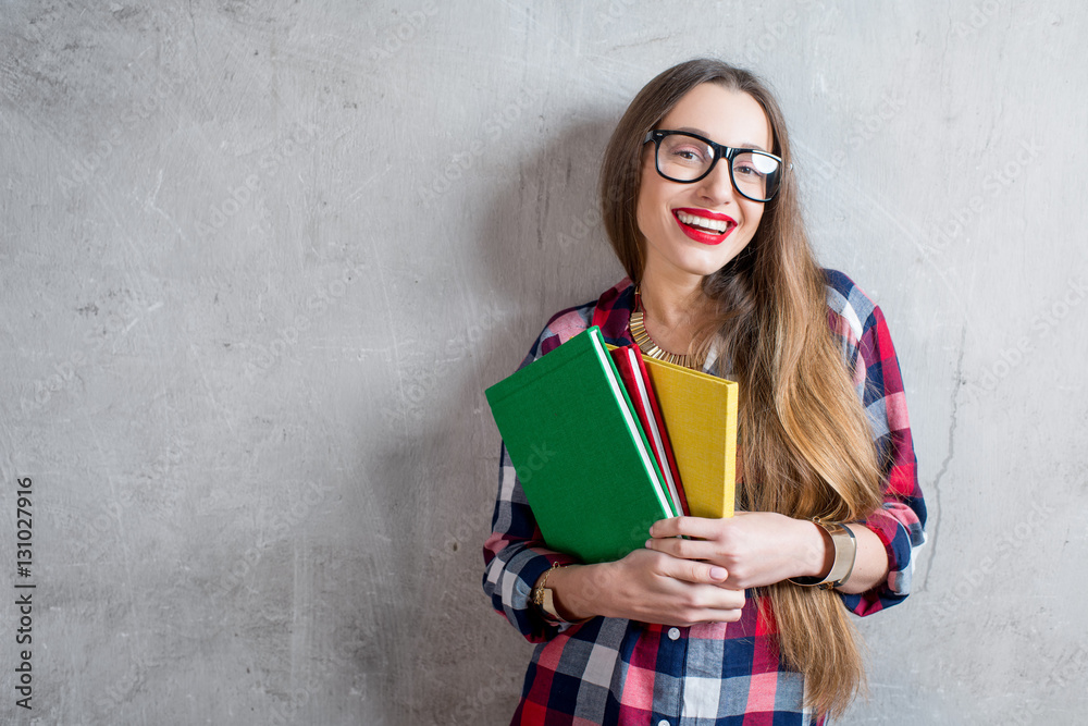 Portrait of a happy young student in checkered shirt with colorful books on the gray wall background