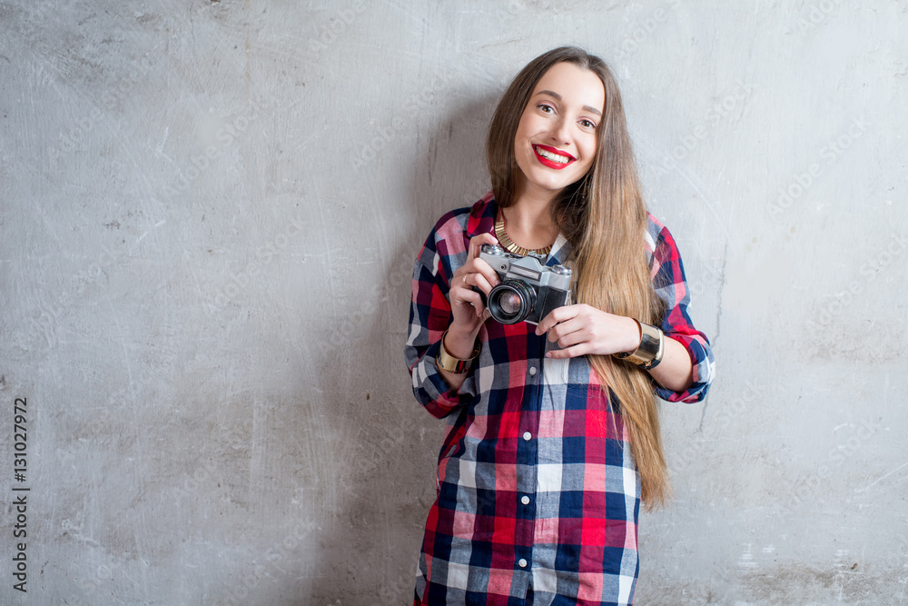 Portrait of young female photographer with retro camera on the gray wall background