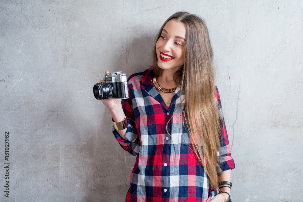 Portrait of young female photographer with retro camera on the gray wall background