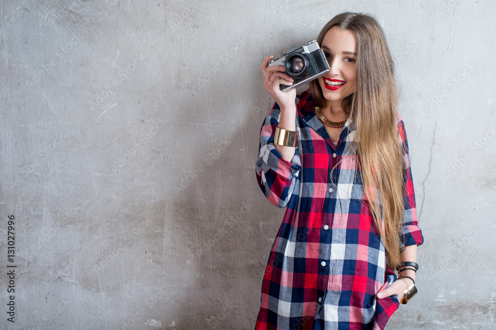 Portrait of young female photographer with retro camera on the gray wall background