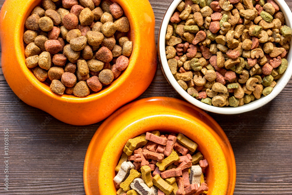 dry dog food in bowl on wooden background top view