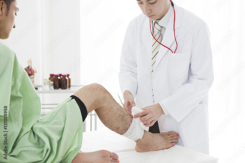 The doctor is wrapping a bandage on the mans right leg