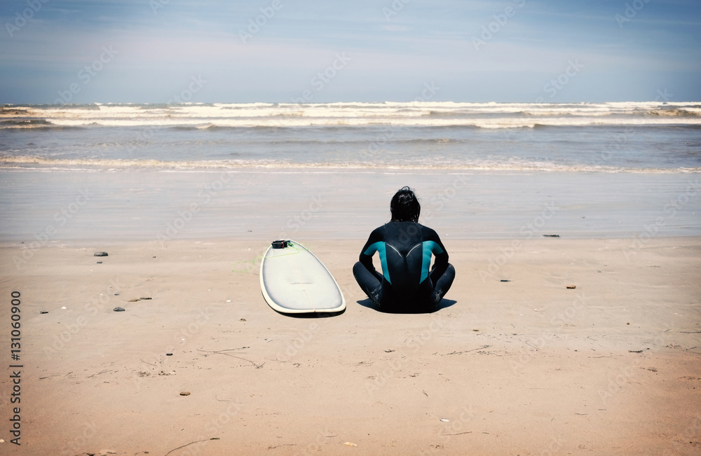 Lone surfer has time to think whilst sitting on a beach in isolation looking at the waves