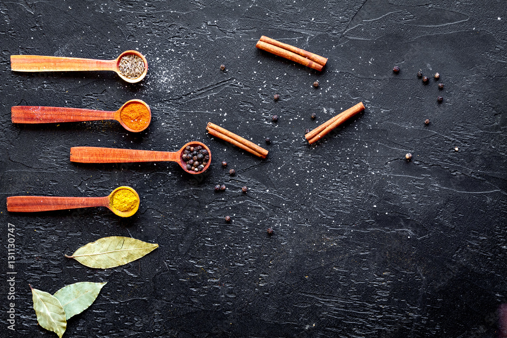 spices in wooden spoons on dark background top view