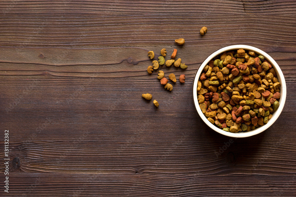 dry cat food in bowl on wooden background top view