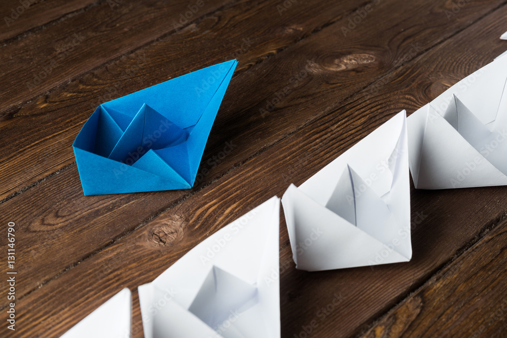 Business leadership concept with white and color paper boats on wooden table