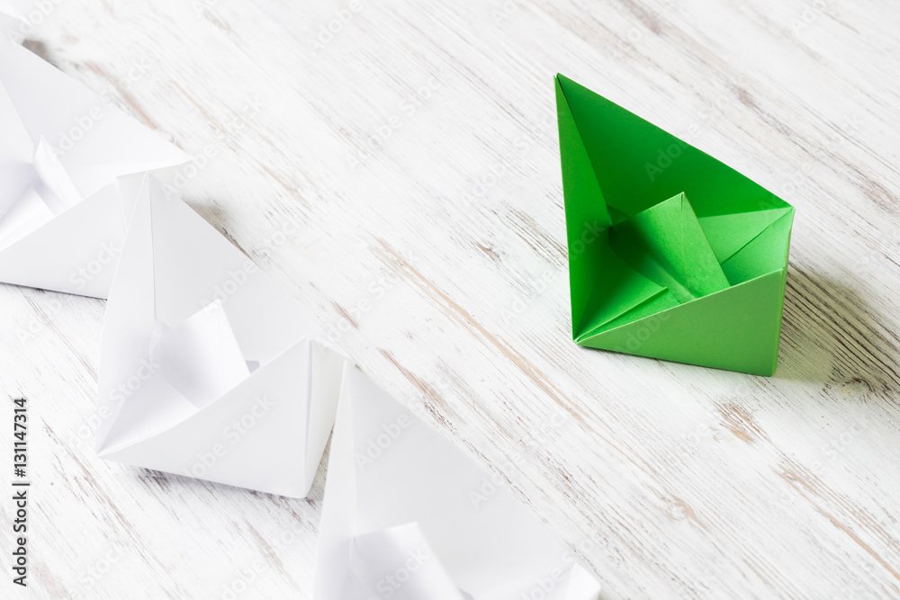 Business leadership concept with white and color paper boats on wooden table