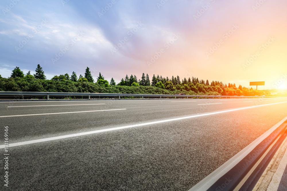 Asphalt road and woods at sunset