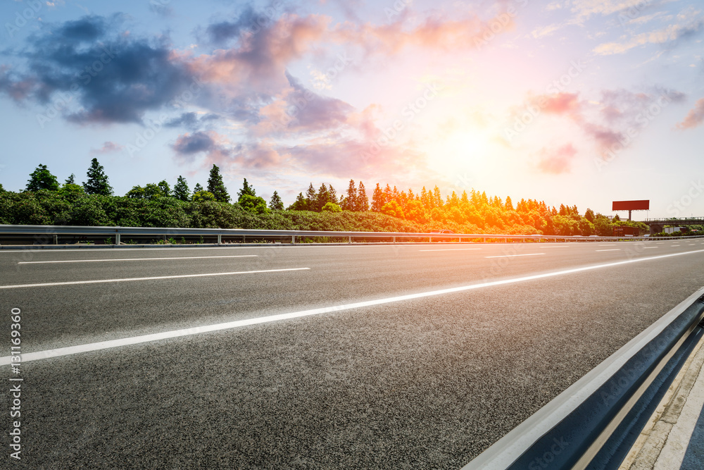 Asphalt road and woods at sunset