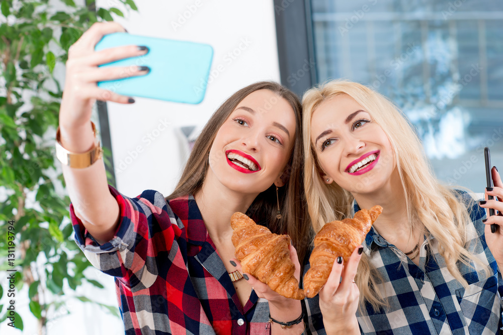 Young female friends dressed casually in checkered shirts taking selfie photo with coffee cups and c