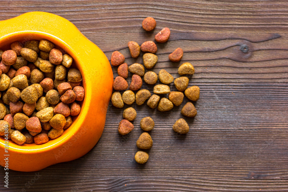 dry cat food in bowl on wooden background top view