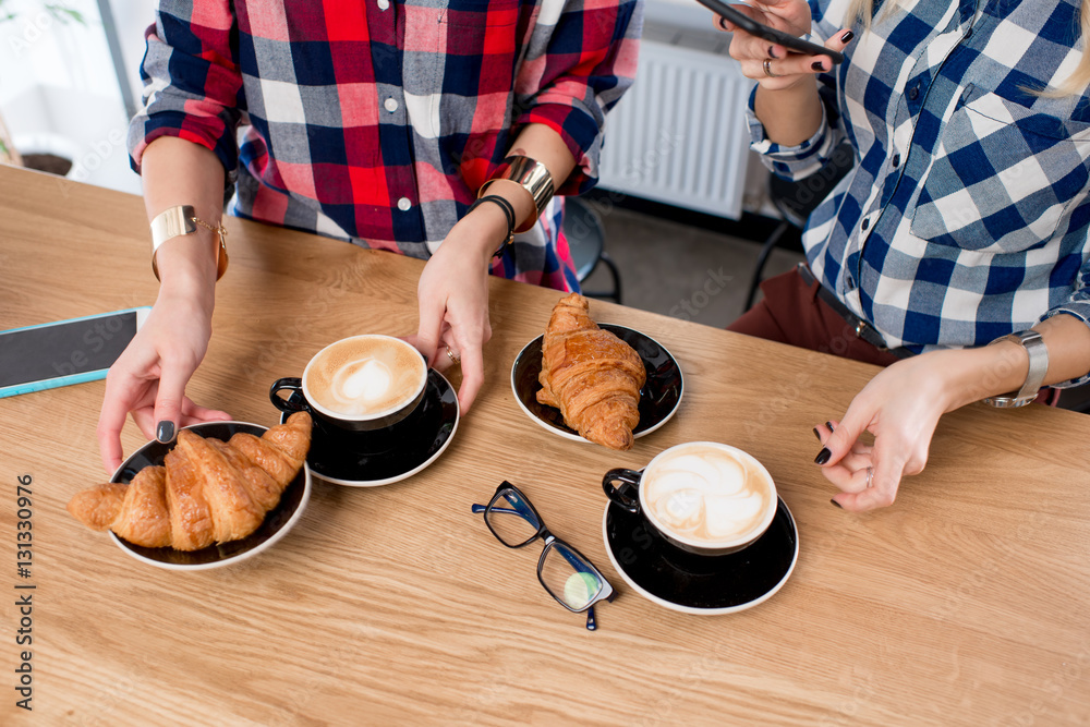 Top view on the wooden table with female hands holding coffee cups and croissants