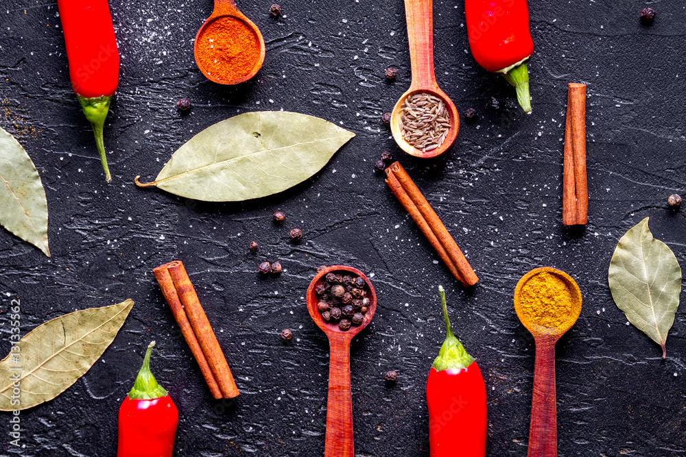 spices in wooden spoons on dark background top view