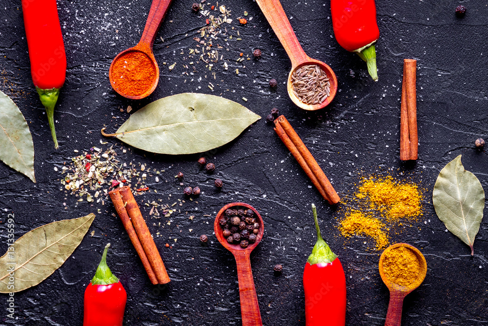 spices in wooden spoons on dark background top view