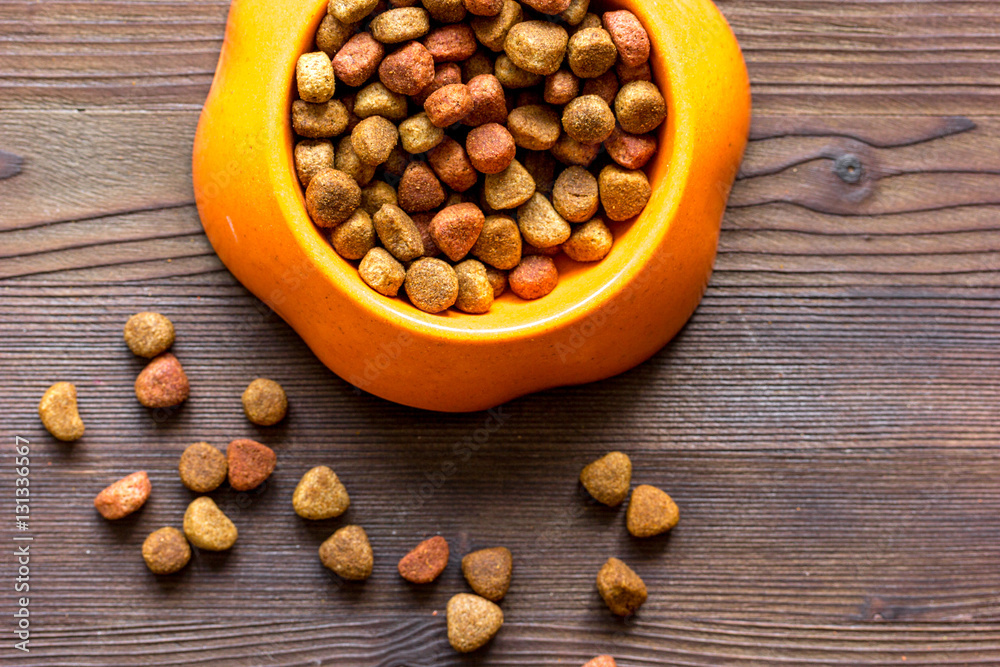 dry cat food in bowl on wooden background top view