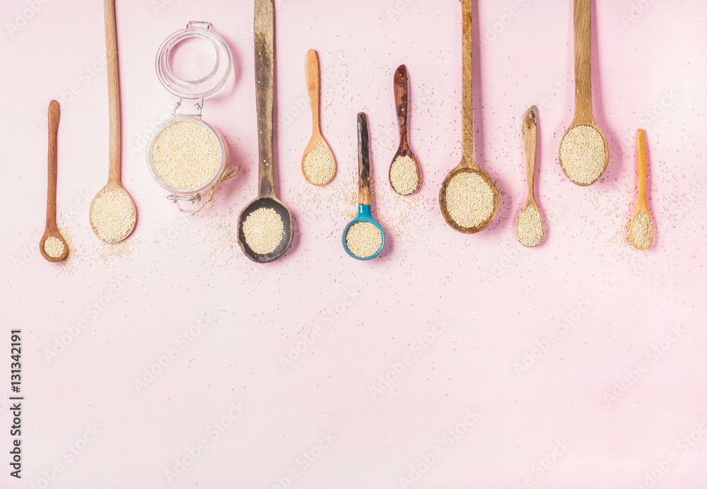 Quinoa seeds in different spoons and glass jar over light pink background, top view, copy space. Sup