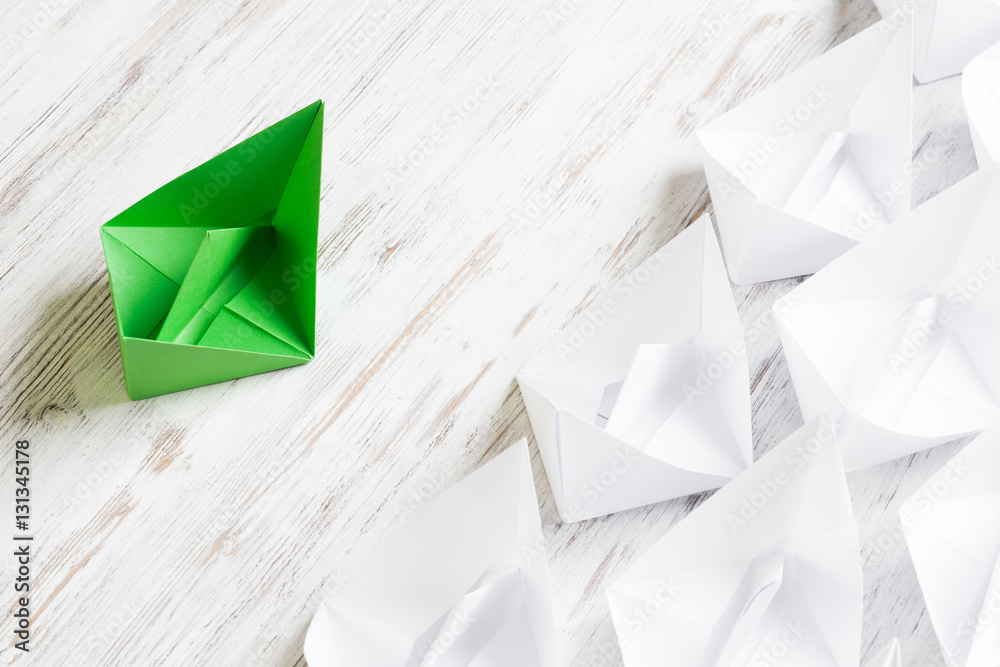 Business leadership concept with white and color paper boats on wooden table