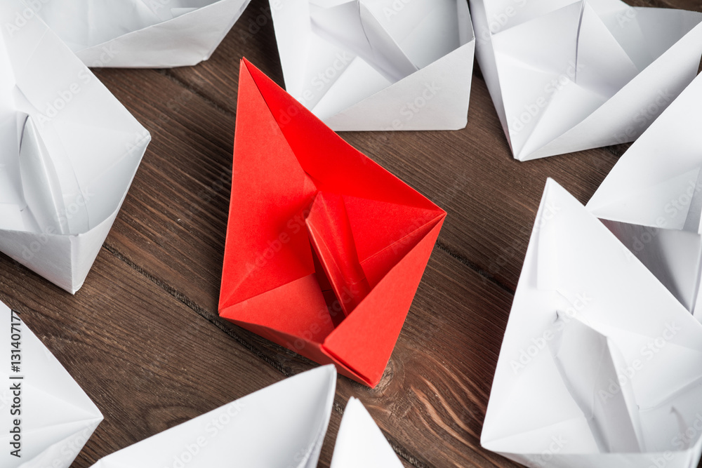 Business leadership concept with white and color paper boats on wooden table