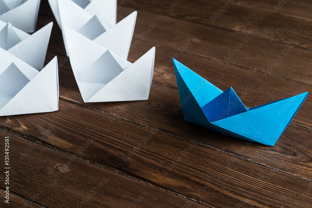 Business leadership concept with white and color paper boats on wooden table