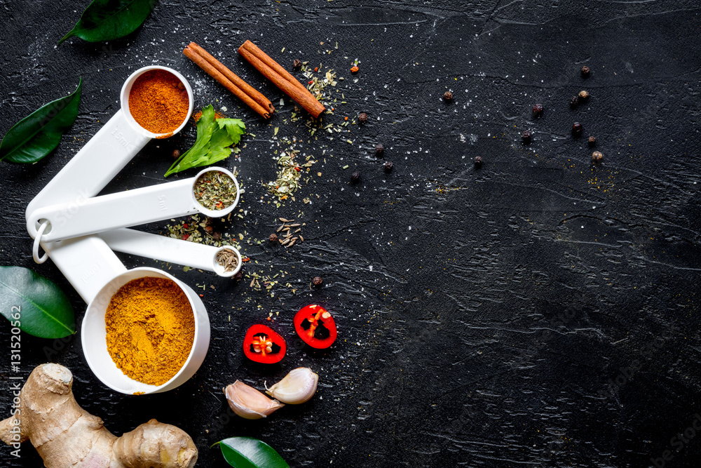 spices in wooden spoons on dark background top view