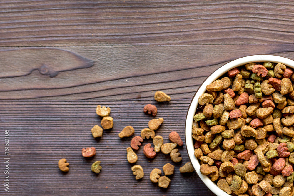 dry cat food in bowl on wooden background top view