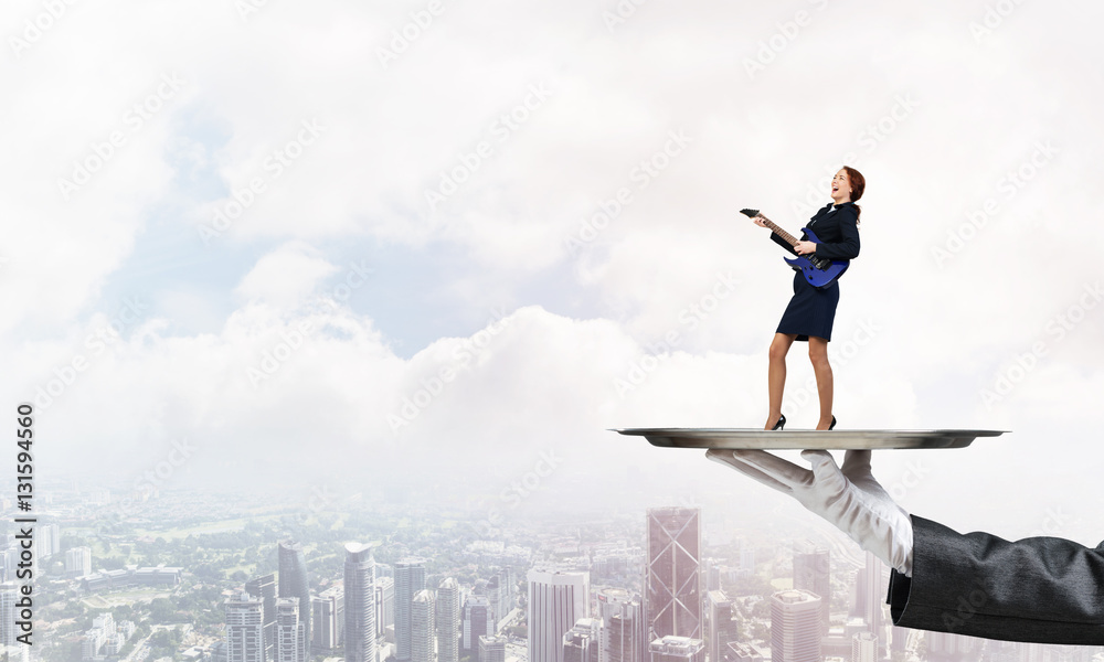 Attractive businesswoman on metal tray playing electric guitar against cityscape background