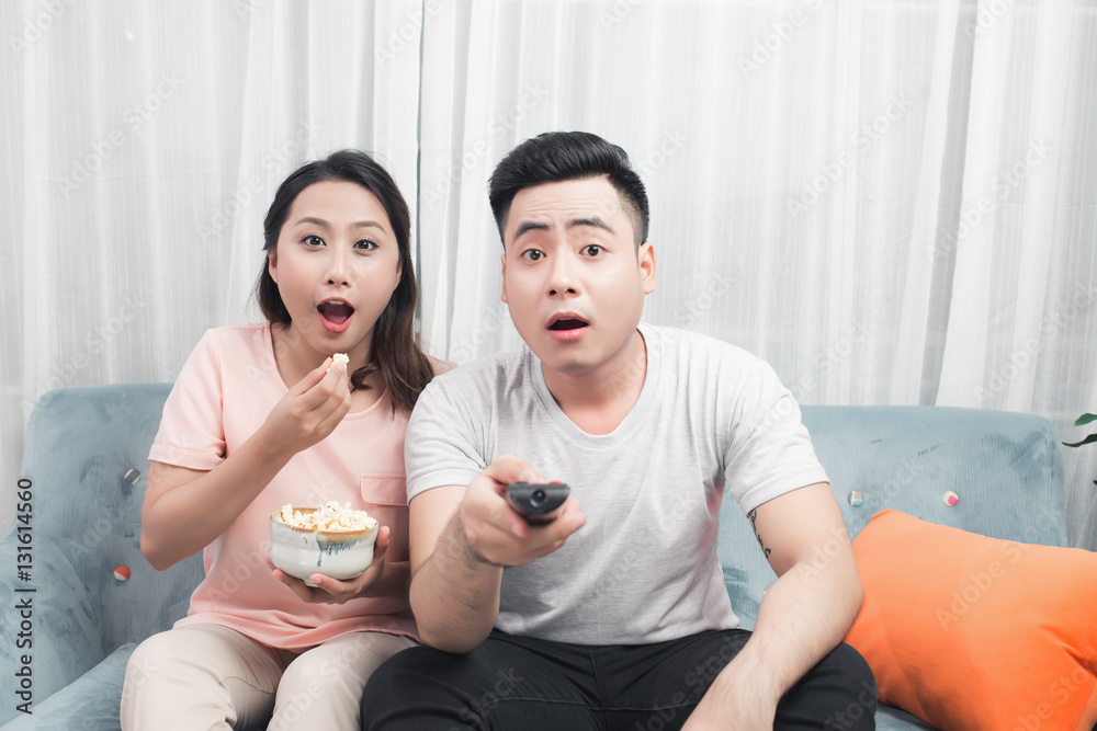 Happy Young Couple In Livingroom Sitting On Couch Watching Movie