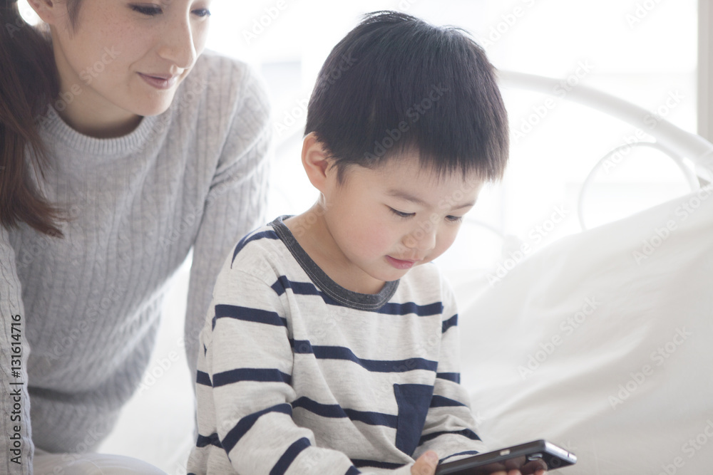 Mother and child are watching smartphone together in the bedroom