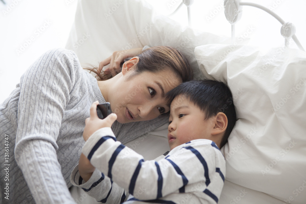 Mother and child are watching smartphone while sleeping in bed